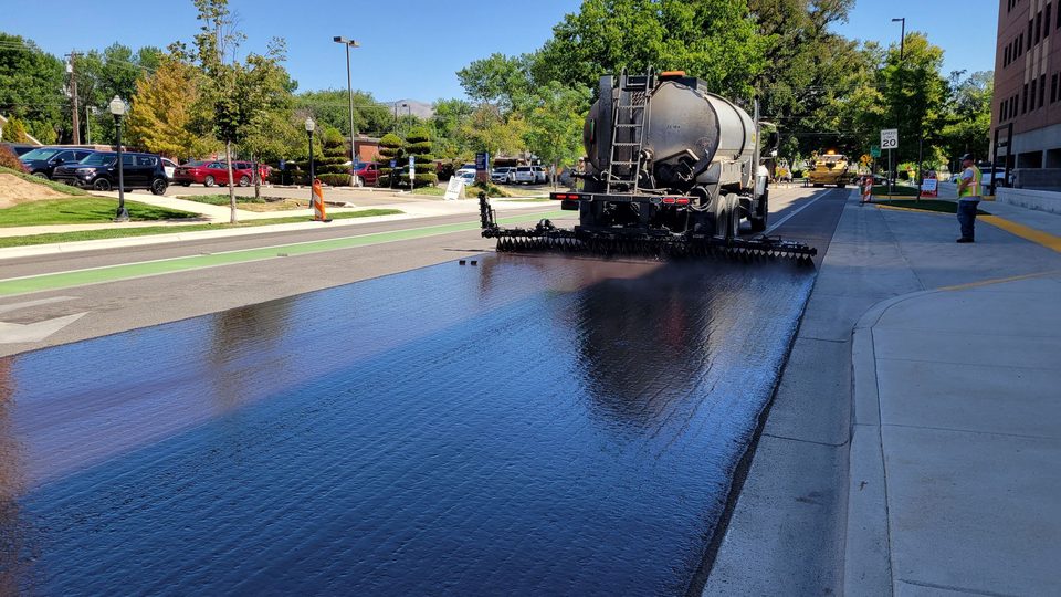 Distributor truck spraying a wet black coat across an asphalt surface